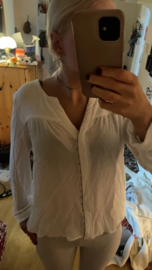 Vit henley-skjorta med knappar - Säljer en vit henley-skjorta med v-ringad hals och guld knappar framtill. Skjortan har långärmade ärmar och är gjord i ett lätt och luftigt bomullsmaterial. Perfekt för dig som gillar en enkel och clean stil.