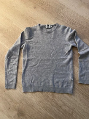 Grå stickad tröja från NN07 - En stilren grå stickad tröja från NN07 i klassisk modell.  Tröjan är gjord av 100% ull. Knappt några tecken på användning, sitter som mer som en XS eller XXS. Ställ gärna frågor vid funderingar! 😊