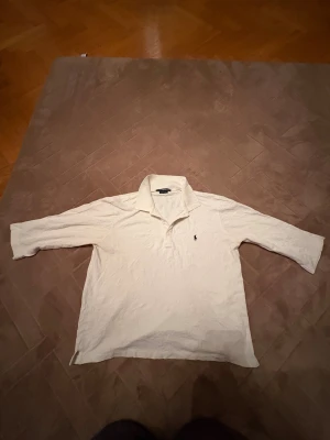 Vit pikétröja från Ralph Lauren Sport - Vit pikétröja från Ralph Lauren Sport med klassisk krage och tre knappar framtill. Tröjan har trekvartsärm och den ikoniska lilla broderade loggan på bröstet. Materialet är mjuk bomull som känns skönt mot huden. Perfekt för dig som gillar clean och stilren look. Perfekt jul klapp !!! Den är inte lång armad men inte kort heller! Mitt i mellan ❤️