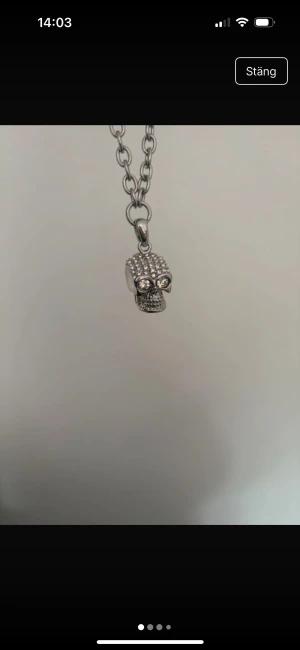 Silverfärgat halsband med döskalle från Edblad - Coolt halsband från Edblad i silverfärg med en kedja och ett hängsmycke i form av en döskalle. Döskallen är dekorerad med glittriga stenar som ögon och över hela huvudet, vilket ger en edgy vibe. Perfekt för dig som gillar detaljer med attityd.