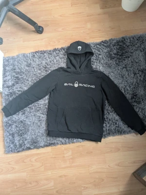 Sail Racing hoodie - En svart sail racing hoodie. Det finns tecken på användning och trycket är lite sprucket men skulle inte säga att det märks. Storleken är S/XS (160cm). Skriv för mer frågor.