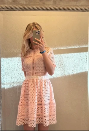 Ljusrosa spetsklänning By Malina - Superfin ljusrosa kortklänning från By Malina med vackert spetsmönster och markerad midja. Klänningen har korta ärmar, rund halsringning och är tillverkad i 100% polyester. Samma modell som kronprinsessan Viktoria hade på prins Oskars dop. 