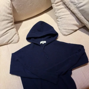  kashmir hoodie från Carmés - Mysig mörkblå hoodie från Carmés i lyxig kashmir. Tröjan har huva med snörning, långa ärmar och ribbade muddar. Perfekt för dig som vill ha en stilren och skön look med premiumkänsla.