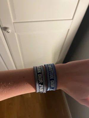 Blå Christian Dior Friendship Armband - Snygga blå och vita friendship-armband från Christian Dior med tydlig logga. Armbanden är vävda i textil och har knytning med tofsar i ändarna. Perfekt accessoar för att ge din outfit en cool och lyxig touch. Passar dig som gillar designer och streetstyle.