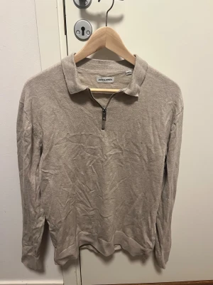 Beige half zip-tröja Jack & Jones - Beige långärmad tröja från Jack & Jones med klassisk krage och half zip-dragkedja framtill. Tröjan är i mjuk bomull och har en enkel, stilren look som passar perfekt till jeans eller chinos. Andvänt max en gång och inga fläckar eller något sånt som jag har hittat på tröjan.
