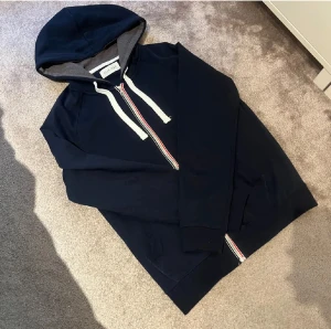 Säljer min snygga pier one hoodie!! - Mörkblå hoodie från Pier One med vit dragsko och hel dragkedja med röd och vit detalj. Grått innerfoder i huvan och två fickor framtill. Perfekt för chill dagar och enkel att matcha med jeans eller joggers.