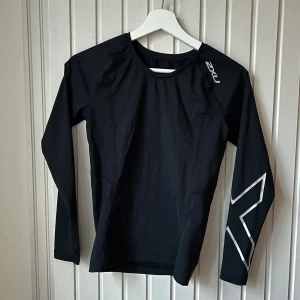 Ny svart träningströja 2XU - Svart långärmat kompressionsplagg från australiensiska 2XU med klassisk X logga på vänster arm. Perfekt för löpning eller gym. Sitter tight, sportplagg med mycket hög kvalitet i nyskick/oanvänd. Passar strl XS34-S36.