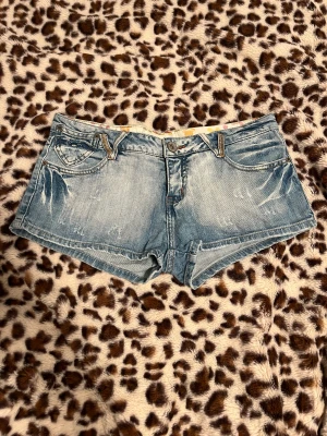 Jeansshorts från Justplay - Snygga ljusblå denimshorts från Justplay med låg midja och klassisk femficksdesign. Köpta på plick och 40 cm rakt över. Shortsen har slitna detaljer och dekorativa sömmar med små nitar på bakfickorna. Perfekt för sommarens chill dagar, med bekväm passform och cool tvätt.