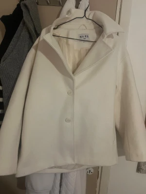 Vit kappa från NA-KD med krage - Säljer en stilren vit kappa från NA-KD med klassisk krage och två knappar framtill. Jackan har raka, långärmade ärmar och är tillverkad i ett mjukt ullmaterial. Perfekt för dig som gillar minimalistisk och clean look. Kappan är använd en del därav att den är nopprig! Men det är inget man tänker på. Jag säljer då jag köpt en svart kappa istället. Finns lite ljusgråa fläckar mot ärmen (rätt svårt att se så inget man tänker på). 