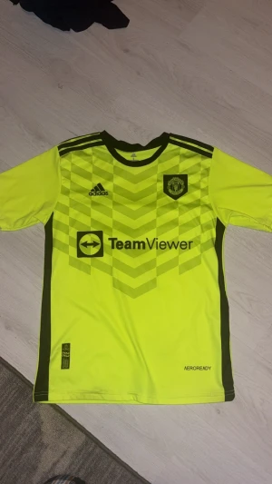 Manchester United Ronaldo 7 fotbollströja - Gul Manchester United fotbollströja från Adidas med svarta detaljer och tryck. Framsidan har klubbmärke, Adidas-logga och TeamViewer sponsor. Baksidan har Ronaldo och nummer 7. Tillverkad i lätt polyester med Aeroready-teknologi och snyggt geometriskt mönster.