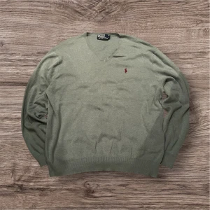 Turkos v-ringad tröja Polo Ralph Lauren - Snygg turkos v-ringad tröja från Polo Ralph Lauren med den klassiska röda logon broderad på bröstet. Tröjan har långärmad passform och är tillverkad i mjuk bomull, perfekt för dig som gillar stilrena och tidlösa plagg.