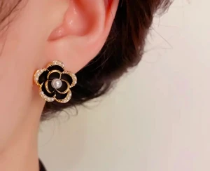 Camellia Svarta blomformade örhängen med pärlor - Supersnygga örhängen i form av svarta blommor med guldfärgade kanter och små vita pärlor längs kronbladen. I mitten sitter en större pärla som ger extra lyxig känsla. Perfekta för dig som vill sticka ut med en elegant och trendig accessoar.