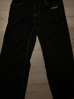 Mörkblåa Spyda jeans med brodyr - Svarta jeans från Spyda med vita kontrastsömmar och broderade spindlar vid fickan. Raka ben och klassisk femficksmodell. Snygg brodyr med Spyda-logga framtill. Perfekta för dig som gillar streetwear och unika detaljer.