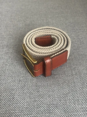 Beige flätat bälte med läderdetaljer - Snyggt beige flätat bälte med bruna läderdetaljer och mässingsfärgat spänne. Perfekt accessoar för att lyfta din outfit med en stilren touch. Passar till både jeans och chinos. De är 85cm långt. De är ifrån volt och kostar 399 nytt.