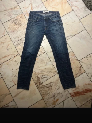 Mörkblå slim fit jeans från dressmann - Säljer ett par mörkblå slim fit jeans med klassisk femficksdesign och snygga slitningar. Jeansen har dragkedjegylf och kontrastsömmar. Perfekta för en avslappnad och trendig look. Har ett litet hål på vänster ben som syns på sista bilden annars inga problem.