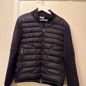 Mörkblå moncler cardigan - Snygg mörkblå cardigan av märke moncler med quiltat mönster framtill och stickade ärmar samt rygg. Jackan har dragkedja framtill, två fickor med dragkedja och ribbad krage. Perfekt för dig som vill ha en sportig, stilren och grisch look. Har ni några frågor är det bara att ställa de😊🫡