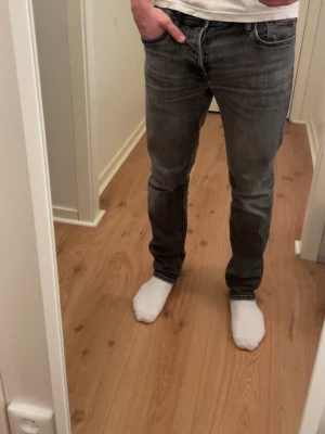 Grå slim fit jeans - Säljer ett par grå slim fit jeans med klassisk femficksdesign och raka ben. Jeansen har en snygg tvättad look och normal midja. Perfekta för dig som gillar en stilren och enkel stil.