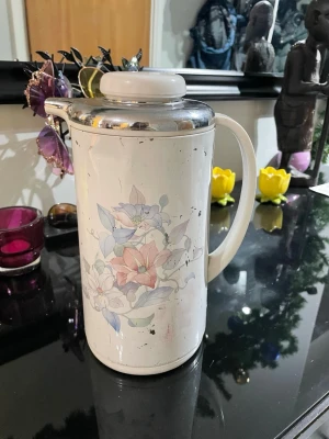 Blommig  Tiger termoskanna  - Säljer en vintage från 1990termoskanna Tiger märket med handtag och lock i plast och metall. Kannan har ett blommigt mönster i pastellfärger med rosa, blå och lila toner. Perfekt för att hålla drycker varma eller kalla under längre tid. Klassisk design som passar i de flesta kök.