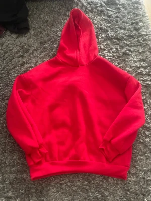 Röd hoodie med spindeltryck - Riktigt fet röd hoodie med stor svart spindel och vitt spindelnät på ryggen samt texten 'SCREAM' i metallstil. Hoodien har huva och ribbade muddar vid ärmar och midja. Perfekt för dig som gillar streetwear och vill sticka ut. Materialet känns mjukt och skönt.