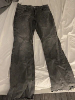 Gråa bootcut jeans med rå kant - Säljer ett par gråa bootcut jeans med råa, fransiga benslut. Jeansen har klassisk femficksdesign och en tvättad look som ger en avslappnad vibe. Perfekta för dig som gillar en lite mer retro och edgy stil.