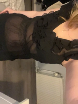 Svart transparent blus med volanger - Snygg svart blus i transparent material med volangdetaljer längs ringningen. Blusen har v-ringad hals och korta ärmar. I fint skick