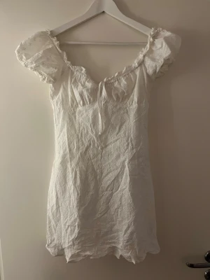 Vit klänning med puffärmar - Söt vit klänning med puffiga kortärmar och urringning. Klänningen har en liten rosett framtill. Broderade mönster och använd en gång