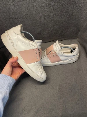 Valentino Garavani - Säljer ett par snygga Valentino Garavani sneakers i vitt skinn med ett ljusrosa band över mitten. Perfekt för en stilren look till vardagen på sommarn, höst och våren. Nypris 8000. Storleken är 40. Skorna har används några gånger och har tecken på användning. OG medföljer samt box, dustbag och kvitto.                                                             Skriv vid frågor, pris kan diskuteras 🤝