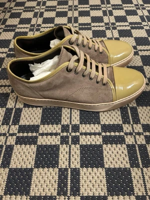 Lanvin - Lanvin i beige mocka med glansig, ljusgul lackad tå och matchande kant. Klassisk låg modell med beige snörning och gummisula. Perfekta för dig som vill ha en unik twist på vardagslooken.