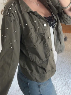 Mörkgrön jacka med nitar - Snygg militärgrön jacka/ overshirt med silverfärgade nitar på axlar och ärmar. Jackan har två bröstfickor med lock, klassisk krage och knappar framtill. As snygg till våren💞