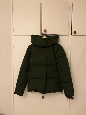 Mörkgrön pufferjacka med huva - Säljer en mörkgrön pufferjacka med stor huva! Jackan har en boxig passform och både dragkedja och knappar framtill💕vänstra fickan är lite trasig (sista bilden), men det är nog lätt att laga 🥰