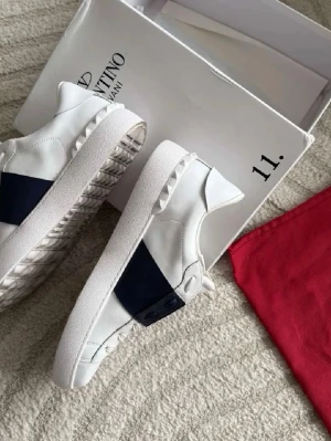Valentino Opens - Snygga vita sneakers från Valentino Garavani med en bred svart rem över sidan och coola nitar på sulan. Orginalbox tillkommer 