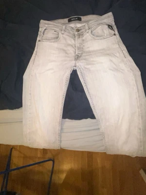 Replay ljusgrå jeans tapered fit - Säljer ett par ljusgrå jeans från Replay med klassisk femficksdesign och snygga detaljer på bakfickorna. Jeansen har en tapered passform och är tillverkade i mjukt denim-material. Perfekta för dig som gillar stilrena och moderna jeans.