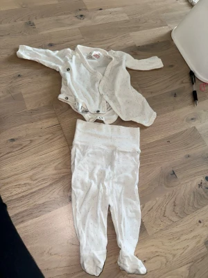 Vitt prickigt babyset med omlottbody H&M Set - Omlottbody och Byxor - Storlek 1-2M - Sött tvådelat babyset i vitt med små grå prickar. Setet består av en omlottbody med tryckknappar och lång ärm samt matchande byxor med fot. Perfekt för mysiga dagar hemma.