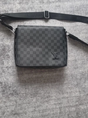 Svart LVaxelväska  - Svart axelväska med klassiskt rutat mönster. Väskan har 3 inre fickor, och 2 ytter fickor. Perfekt accessoar för att lyfta din stil.