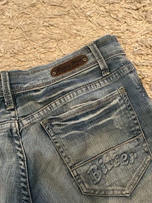 Blå jeansshorts från Bitter Sweet - Säljer ett par klassiska blå jeansshorts från Bitter Sweet med råa kanter och slitna detaljer. Shortsen har knappgylf och broderad logga på bakfickan. Perfekta för en avslappnad stil i sommar. aldrig använd! 