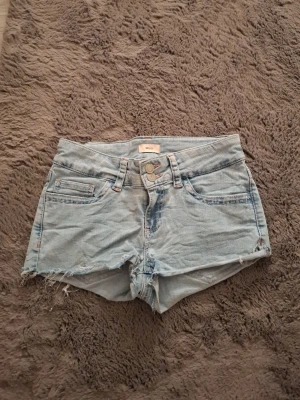 Ljusblå jeansshorts från nelly - Ljusblå jeansshorts från nelly med råa kanter och klassisk femficksdesign. Shortsen har knapp- och dragkedjestängning samt slitna detaljer för en avslappnad look. Perfekta för varma dagar.