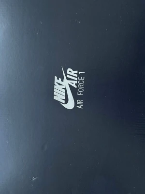 Nike Air Force 1 helsvarta sneakers - Nike Air Force 1 sneakers i helsvart färg med klassisk låg siluett. Skorna har ovandel i mocka och läder, perforerad tå för ventilation och svart sula. Ikonisk Swoosh på sidan och svarta skosnören. Perfekta för en clean och stilren look.