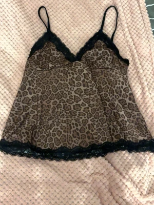 Leopardmönstrad topp med spets - Snygg leopardmönstrad med svarta spetsdetaljer längs urringning och nederkant. Tunt material och smala axelband.
