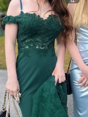 Mörkgrön balklänning med spets och bling! - Elegant mörkgrön långklänning med offshoulder och spetsdetaljer upptill och på släpet!Klänningen har figurnära passform och vackra detaljer. Perfekt för bal eller festliga tillfällen. Använd endast en gång alltså i nytt skick! ☺️💞Minns jag rätt så är den i storlek 34 eller 36 men har passat mig perfekt som är 156cm 💞