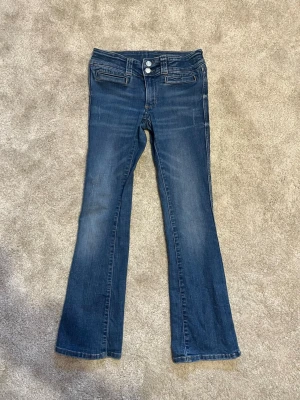 Lågmidjade bootcut jeans - Snygga blå bootcut jeans. Är lite slitna på vissa ställen men det är inget jag tycker att man stör sig på. Midjan är justerbar. Jeansen är väldigt sköna att ha på sig