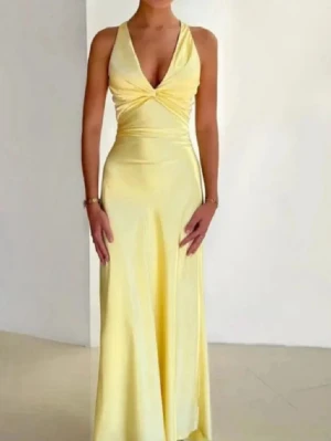 Ljusgul långklänning med öppen rygg - Elegant långklänning i ljusgul satin med djup v-ringning och smala axelband som korsas i ryggen. Klänningen har öppen rygg och en stor rosett baktill i midjan. Perfekt för sommar eller bal.
