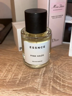 ESSNCE Pink Haze Eau de Parfum - ESSNCE Pink Haze Eau de Parfum har en stilren, genomskinlig glasflaska med svart lock. Doften har fruktiga och blommiga toner med inslag av vanilj, bär, apelsin och karamell. Inspirerad av Viva la Juicy! Perfekt för dig som gillar söta och fruktiga parfymer🩷 Endast testad☺️