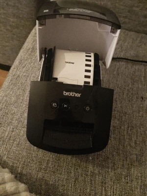 Brother QL-700 etikettskrivare - Säljer en Brother QL-700 etikettskrivare i svart och vit plast. Perfekt för att snabbt skriva ut etiketter till paket, mappar eller organisering. Enkel att använda med tydliga knappar på ovansidan och kompakt design som passar på skrivbordet. Inga etiketter 