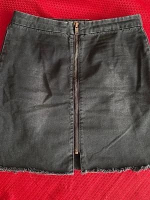 Svart jeanskjol med dragkedja storlek ( 30) S - Cool svart jeanskjol från One by Metasopian X med hög midja och rak passform. Kjolen har en synlig dragkedja framtill och råa kanter nertill för en edgy look. Perfekt att matcha med sneakers eller boots.