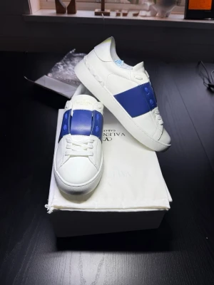 Valentino Garavani sneakers - Ikoniska Valentino Garavani sneakers i toppskick med stilren vit bas och en blå stripe som sätter tonen. En perfekt mix av lyx och street – lowkey flex som funkar lika bra till jeans som till mer uppklädda fits. Premiumkvalitet rakt igenom, tidlös design och den där exklusiva känslan som aldrig går ur stil. Kort sagt, if you know, you know. Fynda idag!