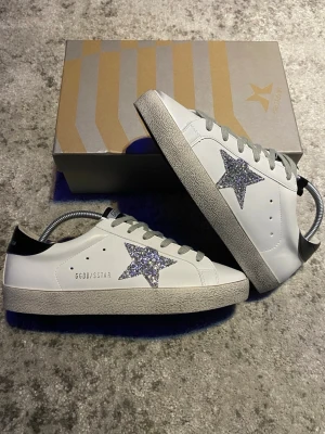 Golden Goose superstar - Ett par riktigt feta GGDB superstar i vit färg med den ikoniska silvriga  stjärnan på sidan. Skorna är storlek 42 och i mycket gott skick, skolåda och lite tillbehöret medföljer självklart👍. Hör gärna av dig med frågor så löser vi något! 😁