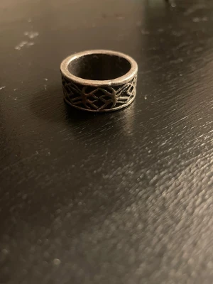 Bred silverfärgad ring med mönster - Cool bred ring i silverfärg med ett detaljerat, genombrutet geometriskt mönster runt hela ringen. Ringen har en robust känsla och passar perfekt för dig som gillar unika accessoarer med lite edge.