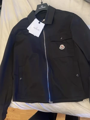 ÄKTA Svart overshirt från Moncler - Svart overshirt från Moncler. Säljer för att den börjar bli för lite för mig. Passar bra om man är 175 cm. Är även öppen för byten mot andra kläder. 