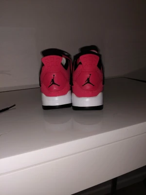 Nike Air Jordan 4 Retro röd/svart - Säljer ett par Nike Air Jordan 4 Retro sneakers i rött, svart och vitt. Skorna har klassisk Jumpman-logga på hälen och en snygg kontrast mellan färgerna. Ovandelen är i syntetmaterial och textil, med snörning framtill och vadderad plös.