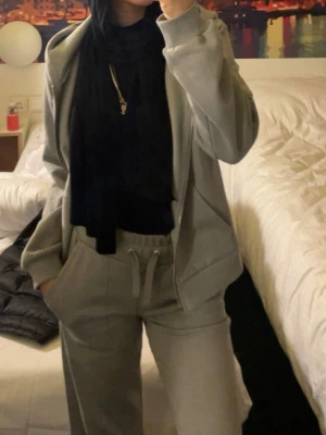 Grått loungewear-set med hoodie - Mysigt grått loungewear-set med dragkedja på hoodien och matchande byxor med dragsko i midjan. Perfekt för chill dagar hemma eller när du vill vara bekväm men ändå snygg. Setet har en avslappnad passform och stora fickor.